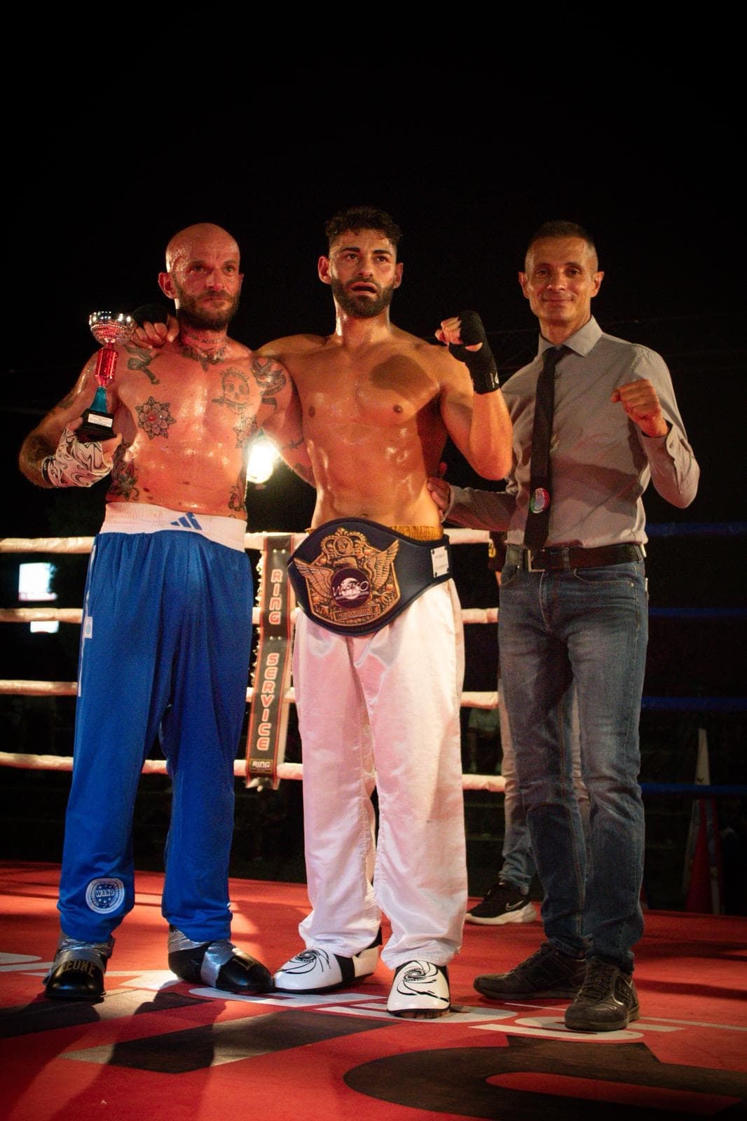Campione IKTA con la cintura del titolo insieme agli ufficiali di gara